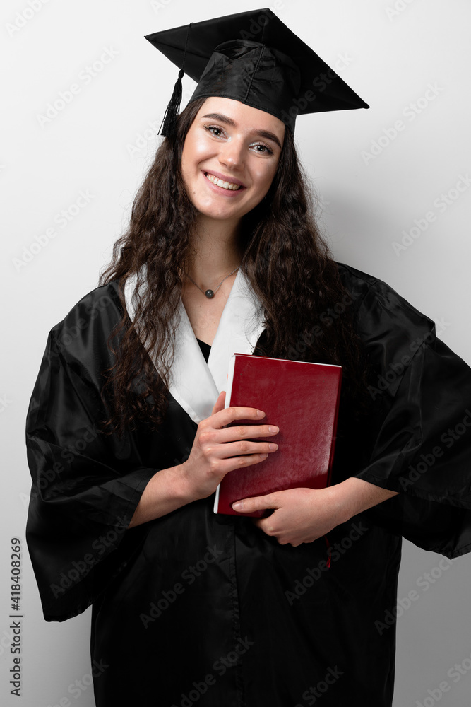Student with book in graduation robe and cap ready to finish college. Future leader of science. Academician young woman in black gown smiling. Student with book in graduation robe and cap ready to finish college. Future leader of science. Academician young woman in black gown smiling.
