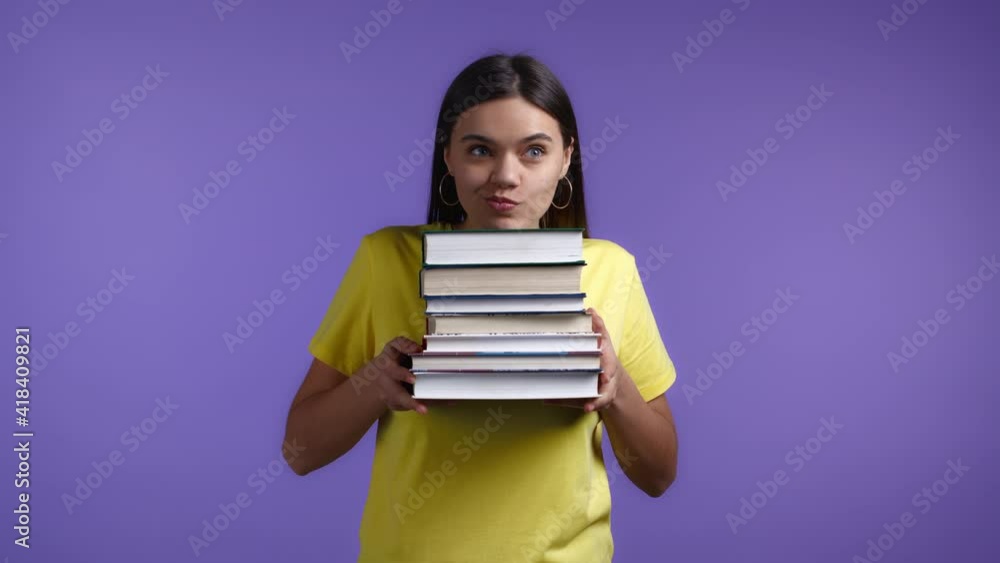 Smiling woman as student on violet background holds stack of university books from library. Girl smiles, she is happy to graduate. Smiling woman as student on violet background holds stack of university books from library. Girl smiles, she is happy to graduate.