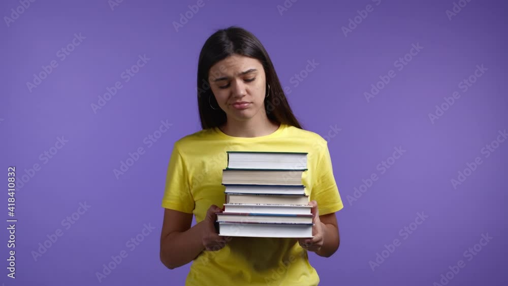 European bored woman as student is dissatisfied with amount of homework and books. She is annoyed, discouraged frustrated by studies. Violet studio background European bored woman as student is dissatisfied with amount of homework and books. She is annoyed, discouraged frustrated by studies. Violet studio background