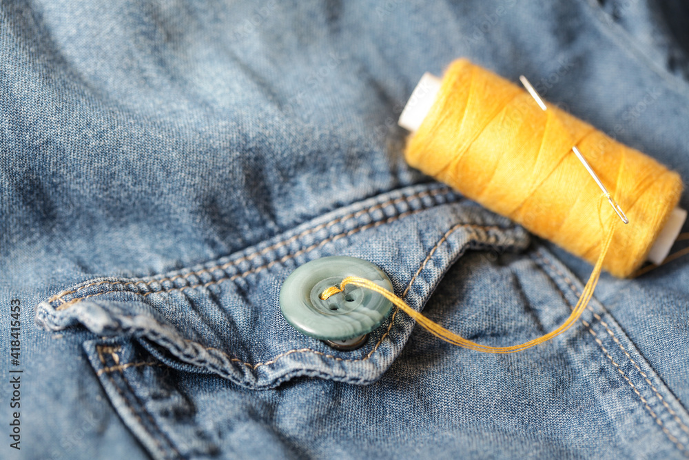 Buttons, Thread and Sewing Needle on Denim. Close-up