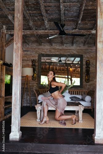 In the interior of the bungalow poses a beautiful girl in a long skirt and top. High quality photo