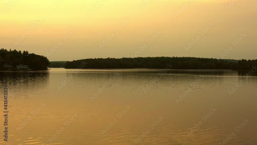 Aerial shot of lake near trees against orange sky at sunset, drone flying forward over water - Berkshire County, Massachusetts Aerial shot of lake near trees against orange sky at sunset, drone flying forward over water - Berkshire County, Massachusetts