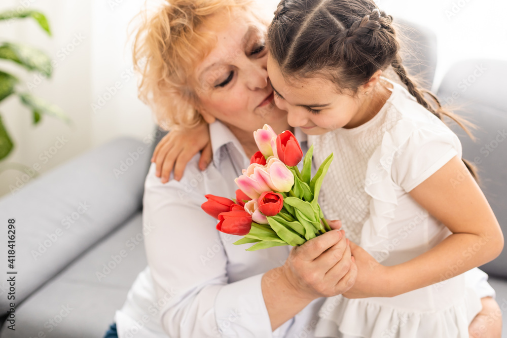 Little beautiful granddaughter gives her grandmother a bouquet of pink tulips. The concept of family, respect, generation, mother, upbringing Little beautiful granddaughter gives her grandmother a bouquet of pink tulips. The concept of family, respect, generation, mother, upbringing