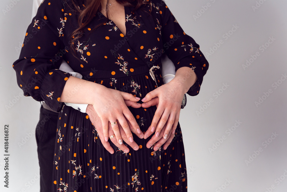 Family in anticipation of a child, a heart on the belly of a pregnant girl. The guy holds the pregnant girl by the belly. Love and relationships on a white background.