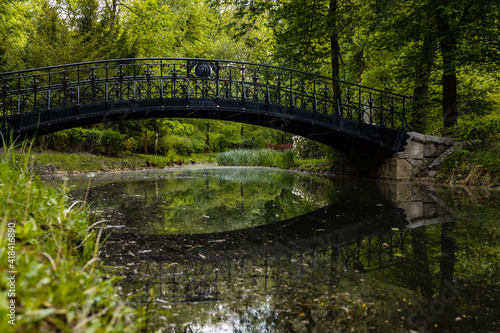 Old wooden bridge with metal railing reflected in silent pond in park