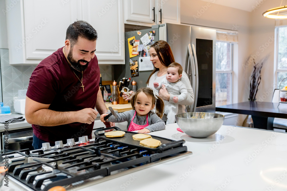Dad making pancakes with toddler daughter, mom holding baby Dad making pancakes with toddler daughter, mom holding baby