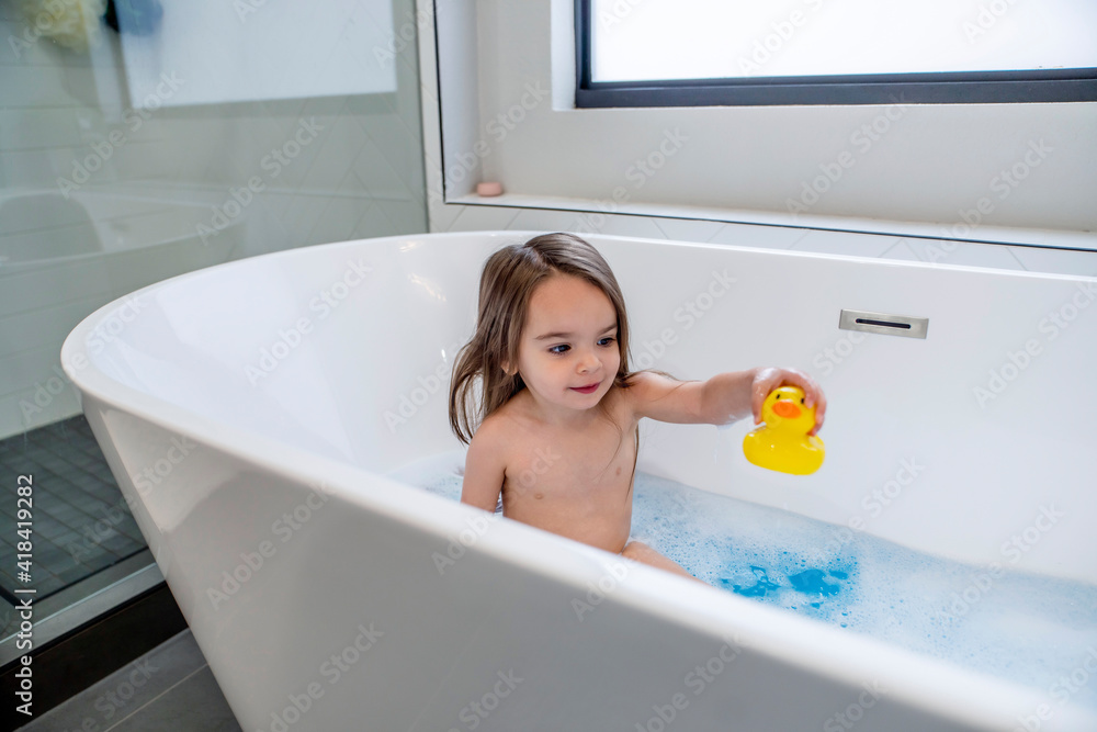 Happy toddler girl playing with rubber duck in bathtub Stock Photo