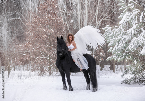 A beautiful curly-haired girl with wings sits astride a Friesian stallion with a long mane