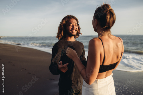 On the wet sand at the edge of the ocean with her back to the camera stands a woman on her looking lovingly smiling man. High quality photo