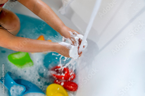 Girl washing soap off of hands in bath water
