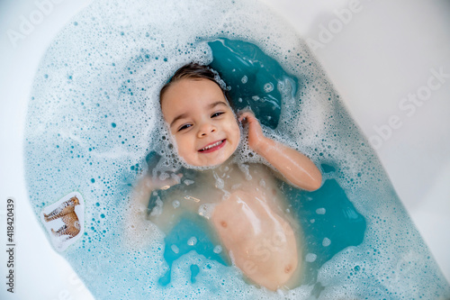 Happy, smiling girl taking bubble bath in bathtub