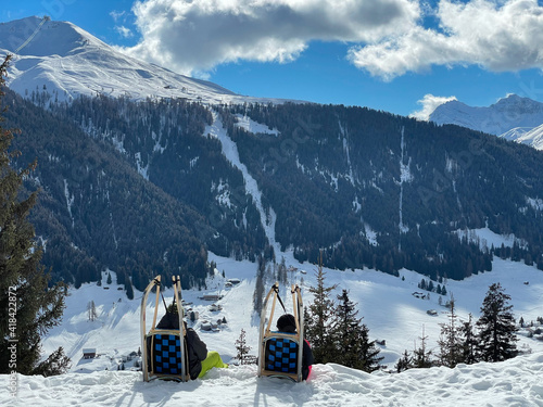 People taking the rest enjoying the landscape of the Alps while sledging in Davos - Schatzalp