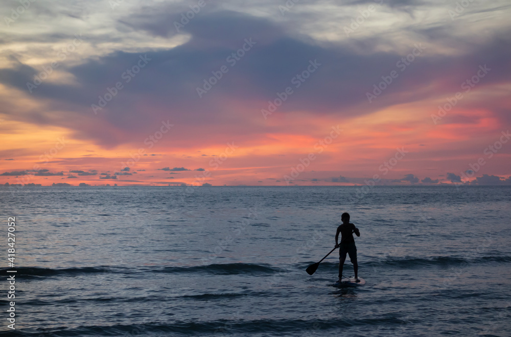 Silhouetted boy standing on a paddleboard watching the sunset