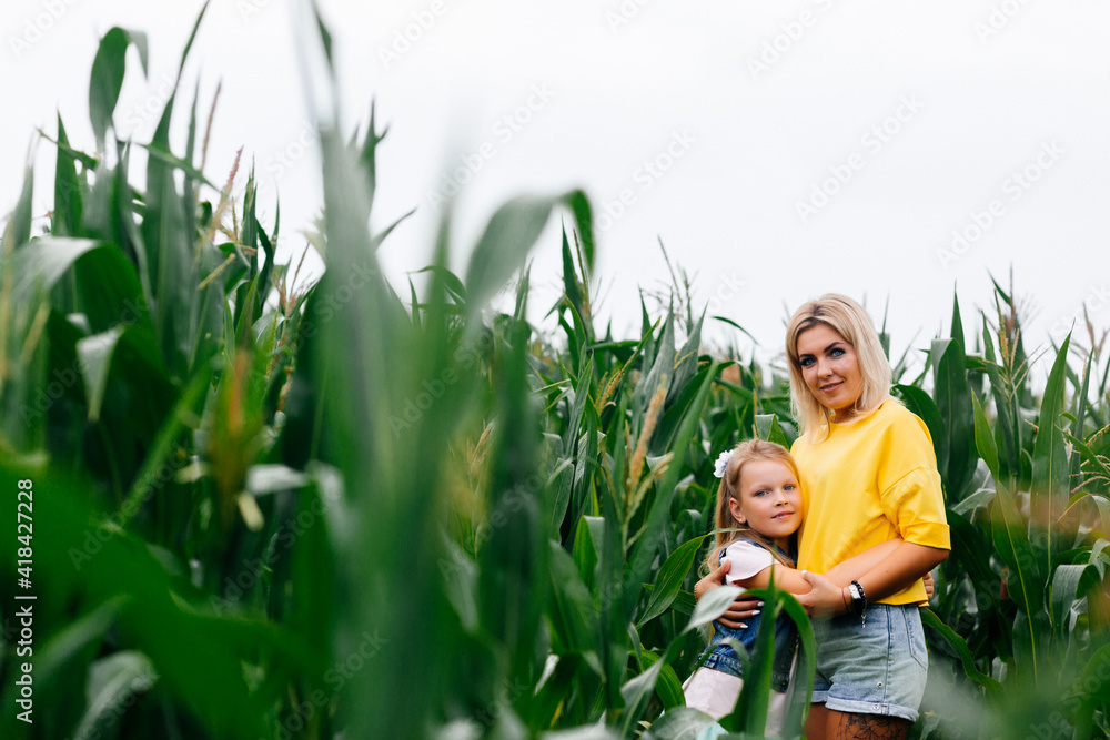 Fototapeta premium Young mother and her daughter in a corn field with green leaves