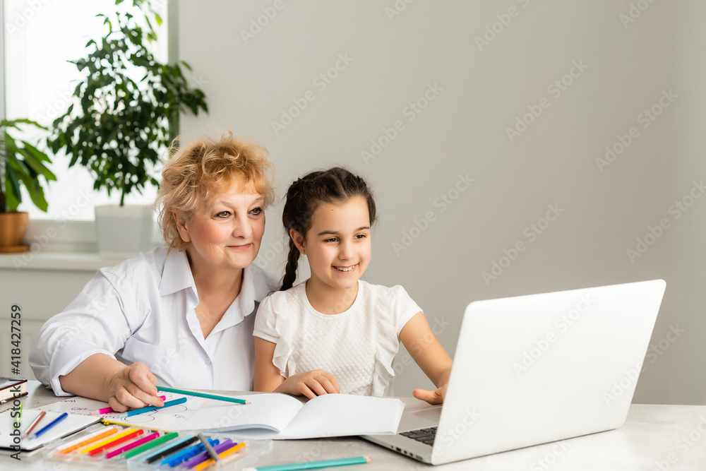 Woman tutor or foster parent mum helping cute caucasian school child girl doing homework sitting at table. Diverse nanny and kid learning writing in notebook studying at home. Woman tutor or foster parent mum helping cute caucasian school child girl doing homework sitting at table. Diverse nanny and kid learning writing in notebook studying at home.