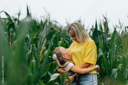 Happy young mother and her daughter in a corn field hug and look at each other