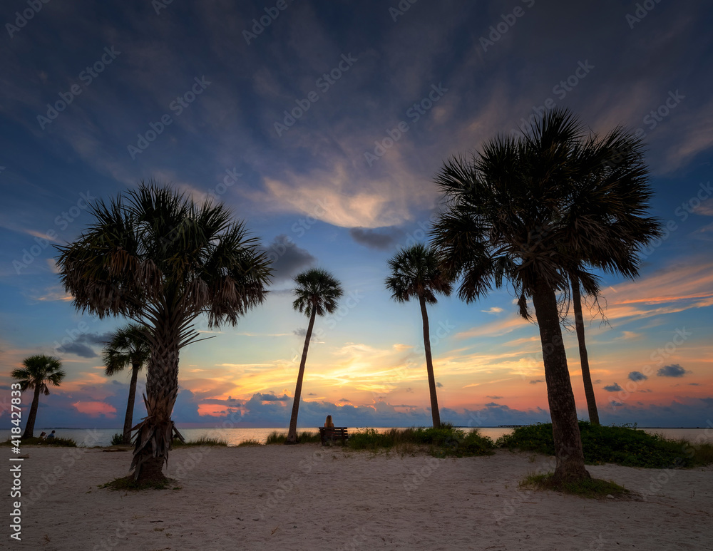 A person sitting on a bench viewing the sunset on the beach in Tarpons Springs, Florida.