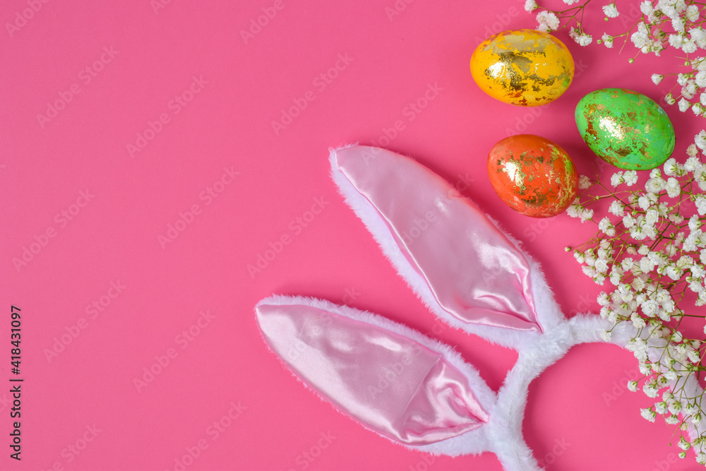 The minimal concept of Easter. An Easter card with a copy of the place for the text. Bunny ears colored eggs and flowers on a pink background. A copy of the space. Top view. Flat lay