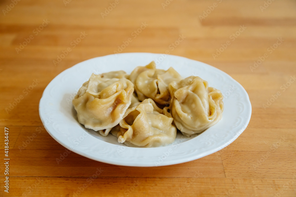 Delicious stuffed dumplings on white plate on wooden table desk. Asian manti or manty of dough and minced with lamb meat, prepared boiled, National traditional Tatar, Kazakh, Uzbek cuisine Delicious stuffed dumplings on white plate on wooden table desk. Asian manti or manty of dough and minced with lamb meat, prepared boiled, National traditional Tatar, Kazakh, Uzbek cuisine