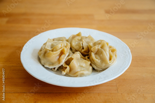 Delicious stuffed dumplings on white plate on wooden table desk. Asian manti or manty of dough and minced with lamb meat, prepared boiled, National traditional Tatar, Kazakh, Uzbek cuisine