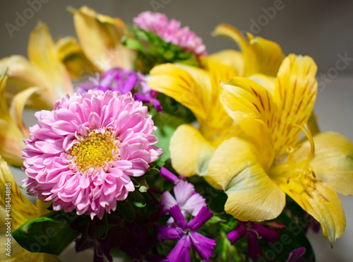 Yellow alstromeria and pink matsumoto asters arranged in a vase on a tile counter. Colorful spring flower arrangement indoors.