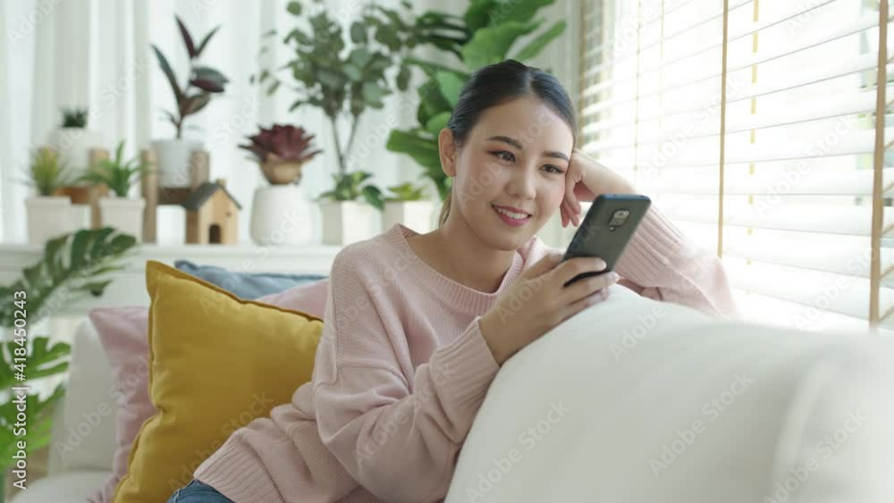 Young attractive beautiful casual asia female lady or student look at cellphone play social media at sofa couch living room feel relax comfort carefree with green houseplant at cozy home apartment. Young attractive beautiful casual asia female lady or student look at cellphone play social media at sofa couch living room feel relax comfort carefree with green houseplant at cozy home apartment.