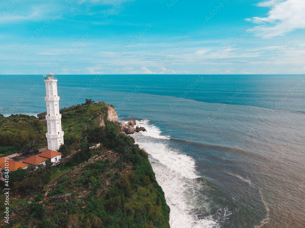Aerial view of Baron Beach in Gunung Kidul, Indonesia with lighthouse and traditional boat.