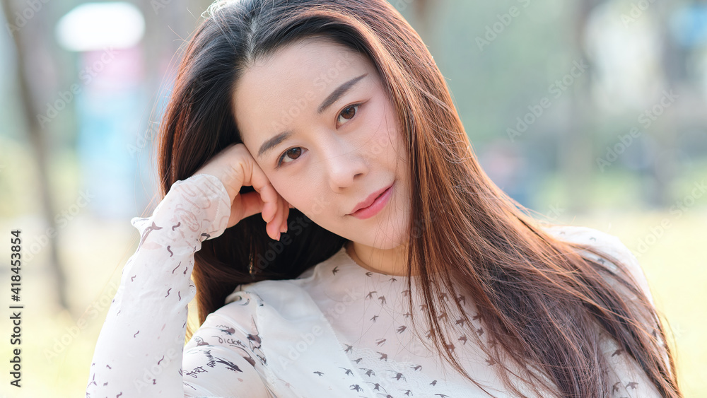 Close up portrait of beautiful young Chinese woman, smiling and looking at camera in sunny day.