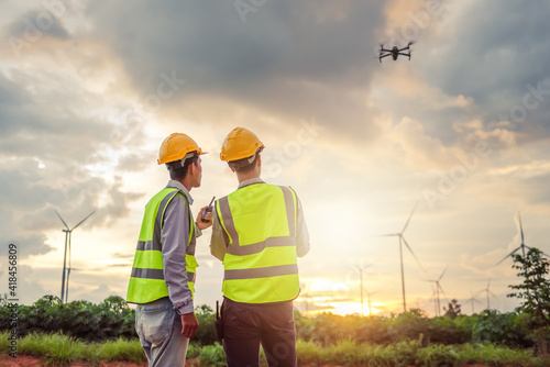 two asian engineers male flying drone surveying and checking wind turbines from the high angle view of the field during beautiful sunset. using drone technology for work. Alternative energy for future