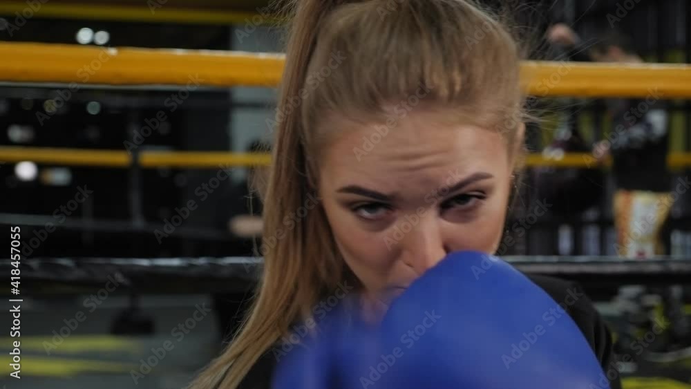 Close-up of a young female boxer in blue boxing gloves practicing a punch in the gym. Close-up of a young female boxer in blue boxing gloves practicing a punch in the gym.