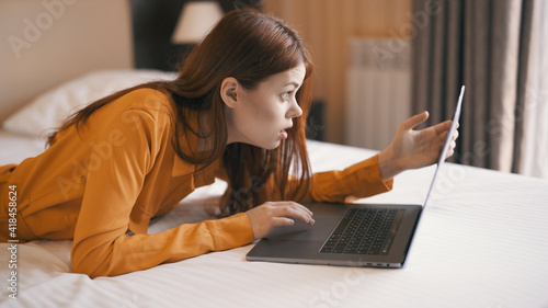 woman lying on bed with laptop working at home communication technology