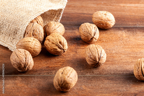 A pile of fresh raw English Walnuts scattered on a wooden table out of burlop vintage  bag. A rustic image  with close up selective focus on walnuts in shell. Angled top view. photo