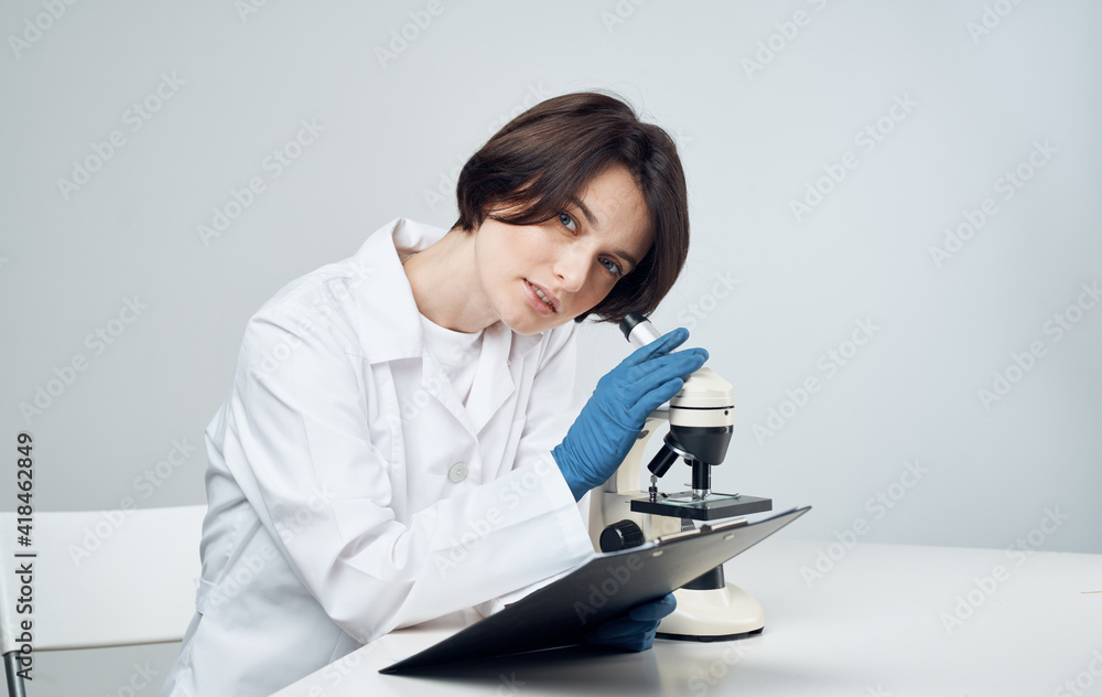 woman doctor in a medical gown with a microscope on the table sits on a chair woman doctor in a medical gown with a microscope on the table sits on a chair