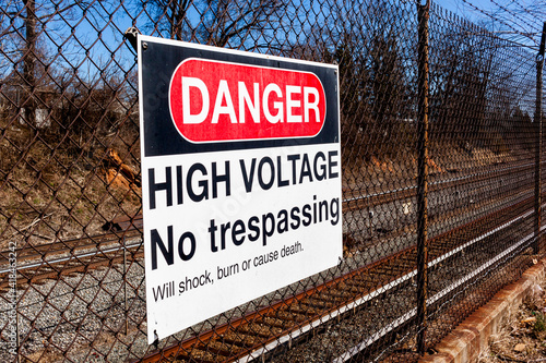 Obraz na plátně Danger, high voltage, no trespassing sign on a fence in front of a rail road