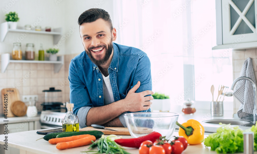 Bearded smiling handsome man in the kitchen at home is posing and looking on the camera Bearded smiling handsome man in the kitchen at home is posing and looking on the camera