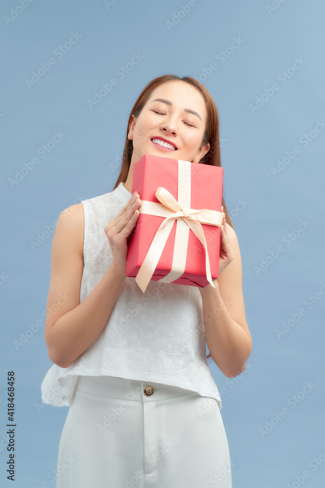 Portrait of a happy smiling girl holding present box isolated over blue background Portrait of a happy smiling girl holding present box isolated over blue background