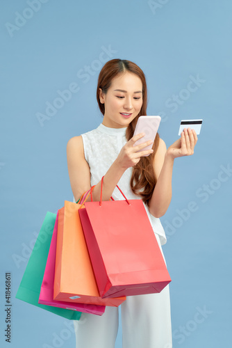 Stylish woman with shopping bag, credit card and phone on the blue wall background. Winter holiday sale