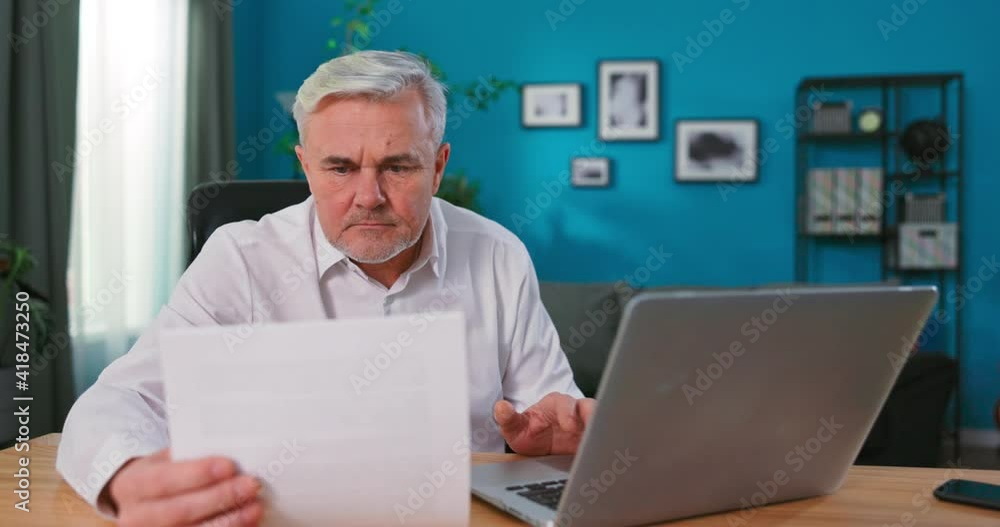Old Senior man checking home finances and bills, he is calculating costs, using computer and writing notes. Elderly Man Reading Documents. Old Senior man checking home finances and bills, he is calculating costs, using computer and writing notes. Elderly Man Reading Documents.