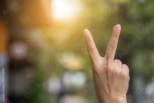Raise two fingers to symbolize peace or victory against a blurry background. © Sawat
