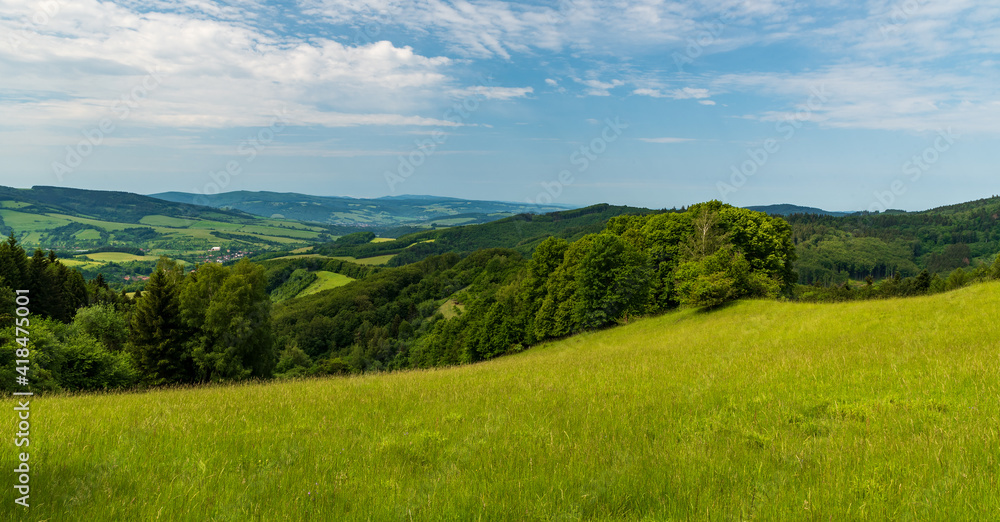 Hilly landscape with meadows, few villages, forest, hills and blue sky with clouds
