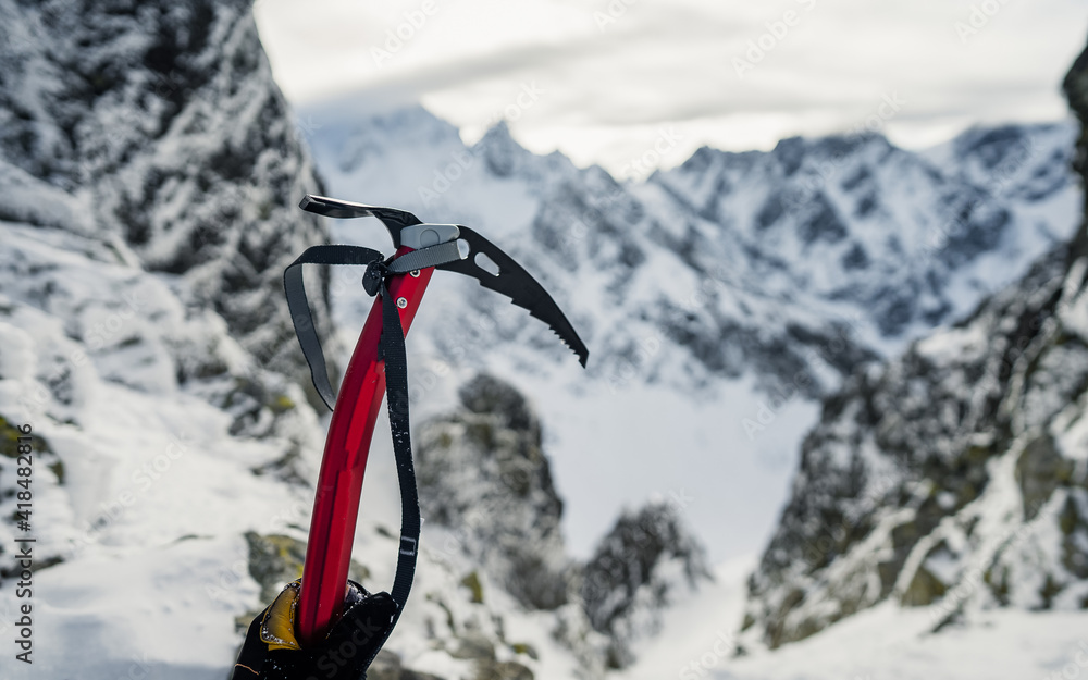 Winter alpine climbing. Hand in a winter glove holding an ice axe, snow