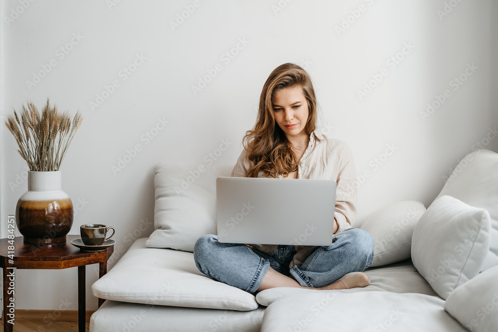 Portrait of a young happy female freelancer sitting on the couch and working on project, watching movie on laptop, studying, blogging, resting and chatting online Portrait of a young happy female freelancer sitting on the couch and working on project, watching movie on laptop, studying, blogging, resting and chatting online