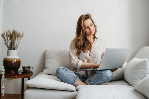 Portrait of a young female freelancer sitting on the couch and working on project, watching movie on laptop, studying, blogging, resting and chatting online