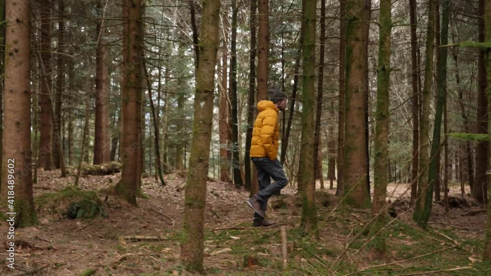 Young european man with bright yellow jacket walks in forest, sideways dolly Young european man with bright yellow jacket walks in forest, sideways dolly