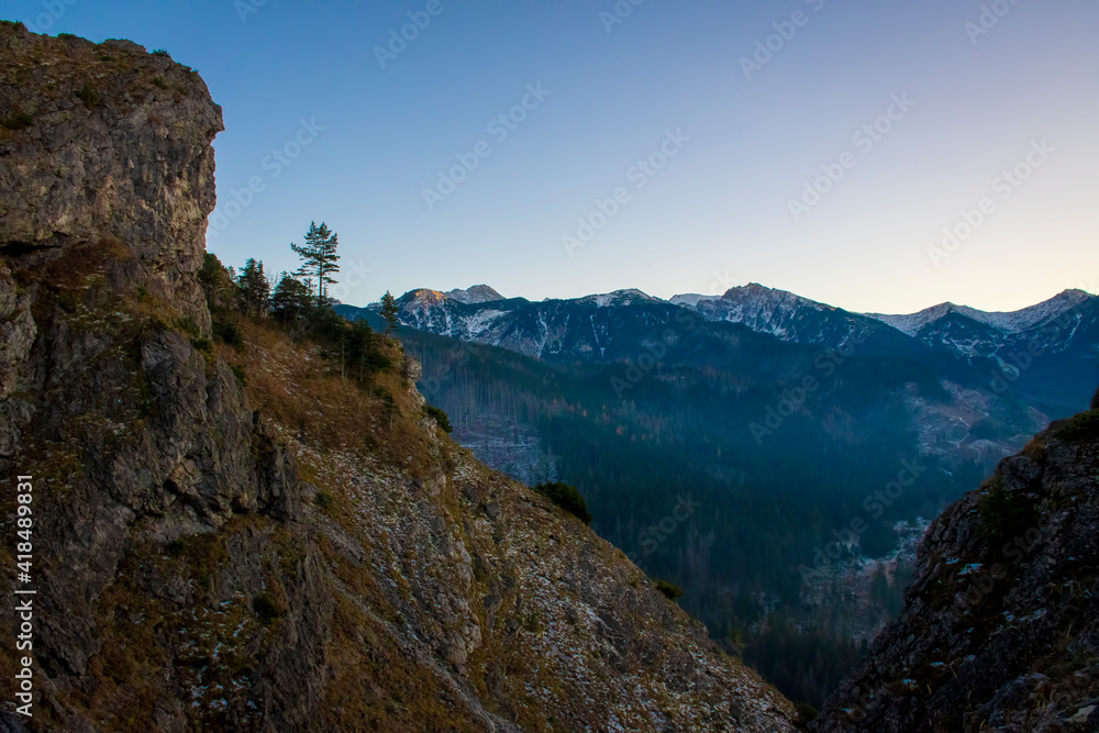 Obraz premium Rock formation on the trail to Nosal Peak, Tatra National Park, Poland. Western Tatras in the distance illuminated by the sunset. Selective focus on the ridge, blurred background.
