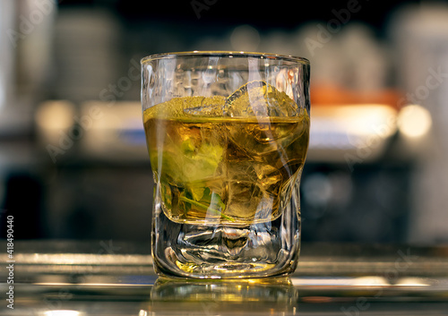 Rum or mojito drink in a glass with ices on a bar counter