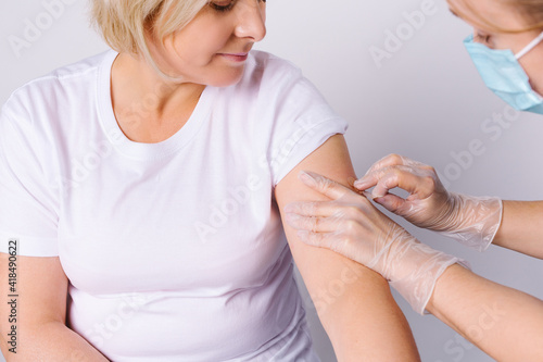 General practitioner vaccinating female patient in clinic. Doctor giving injection to senior woman at hospital. Nurse holding syringe with Covid-19, coronavirus vaccine.