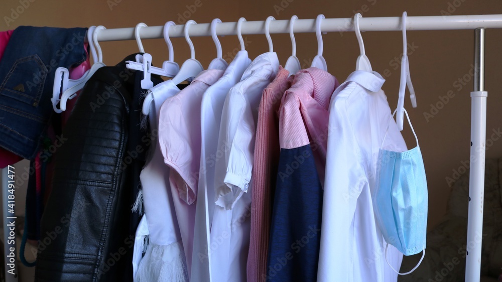 Obraz premium a blue medical mask hangs on a hanger in a women's wardrobe as a necessary accessory for everyday life, children's streetwear on a hanger and a protective mask as part of life in a pandemic