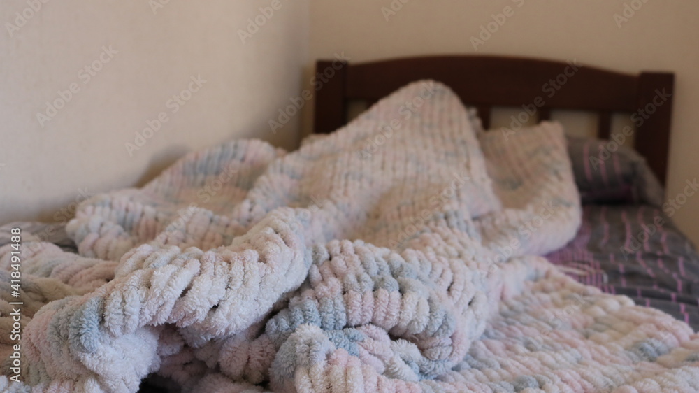 a cozy hand-knitted blanket made of soft white-pink wool is casually crumpled on a wooden bed in a room with light walls, home comfort and a cozy wintertime atmosphere with a woolen homemade blanket a cozy hand-knitted blanket made of soft white-pink wool is casually crumpled on a wooden bed in a room with light walls, home comfort and a cozy wintertime atmosphere with a woolen homemade blanket
