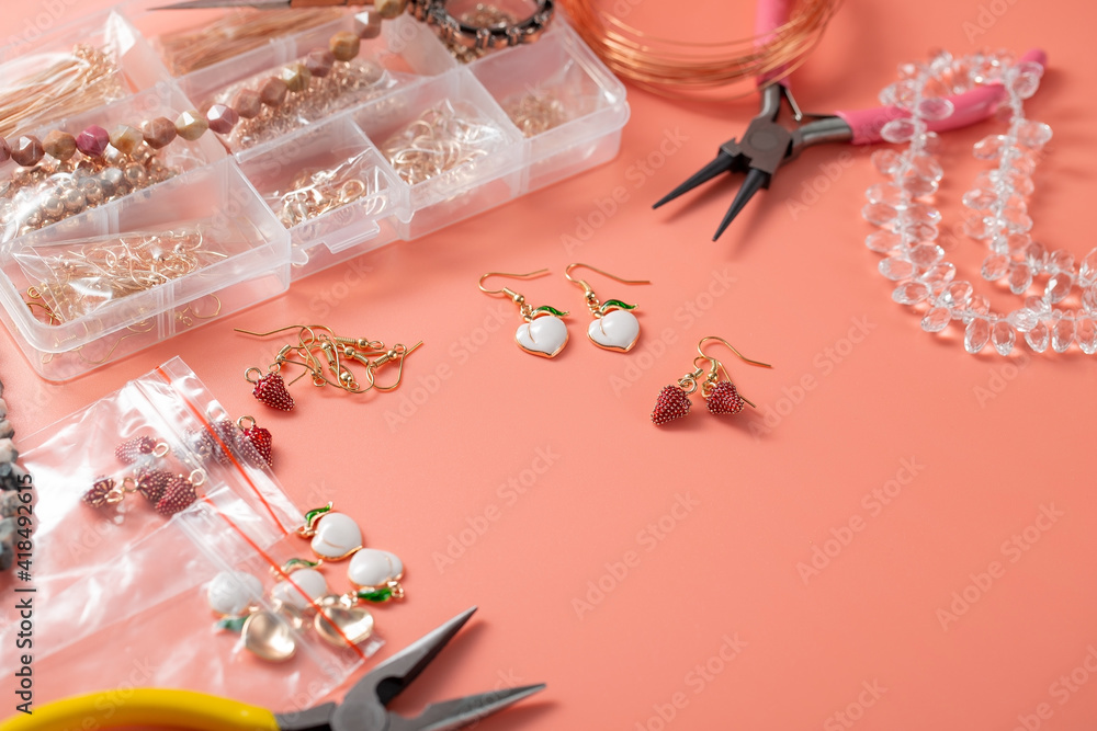 Fototapeta Beautiful accessories and tools for creating handmade jewelry. Metal pendants with enamel in the shape of strawberries, peaches. Pliers, a box of accessories. Copy space for text